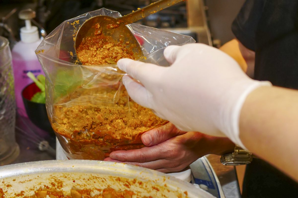 厨房で、手袋をつけて料理を袋に取り分けている手元