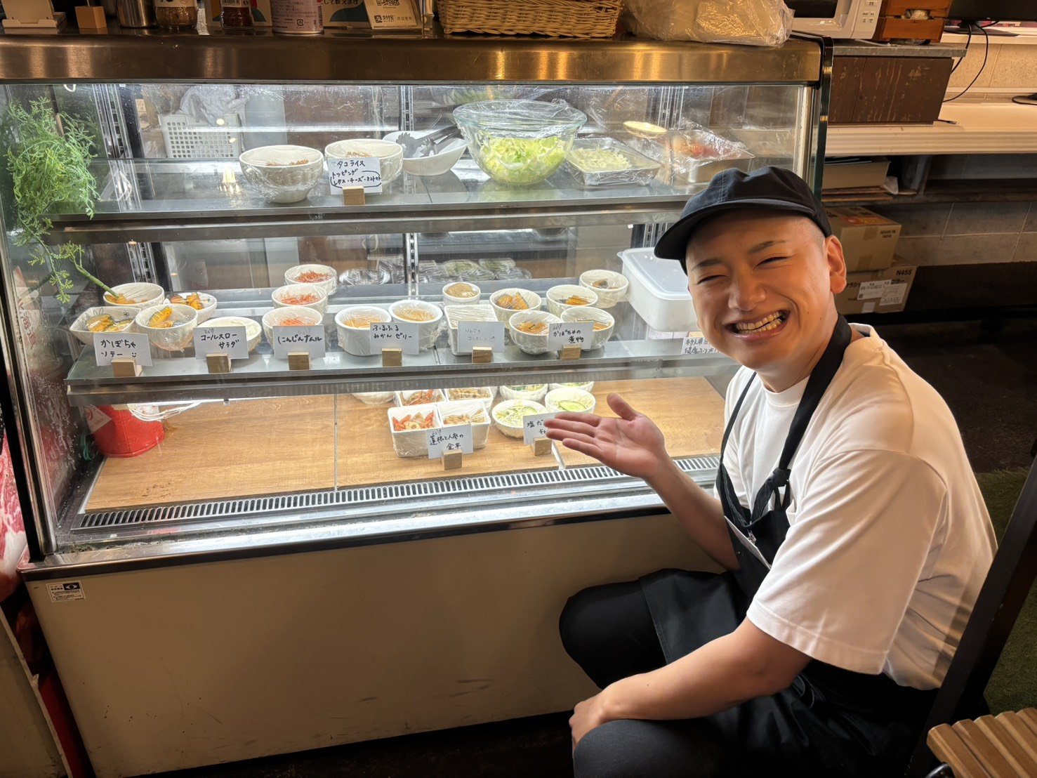 カフェのショーケースの前で、笑顔で料理を紹介するスタッフ